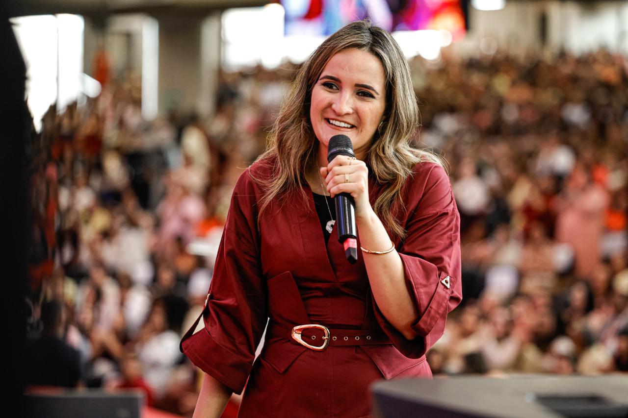 Marinna Ferreira sorrindo, microfone na mão, diante da congregação